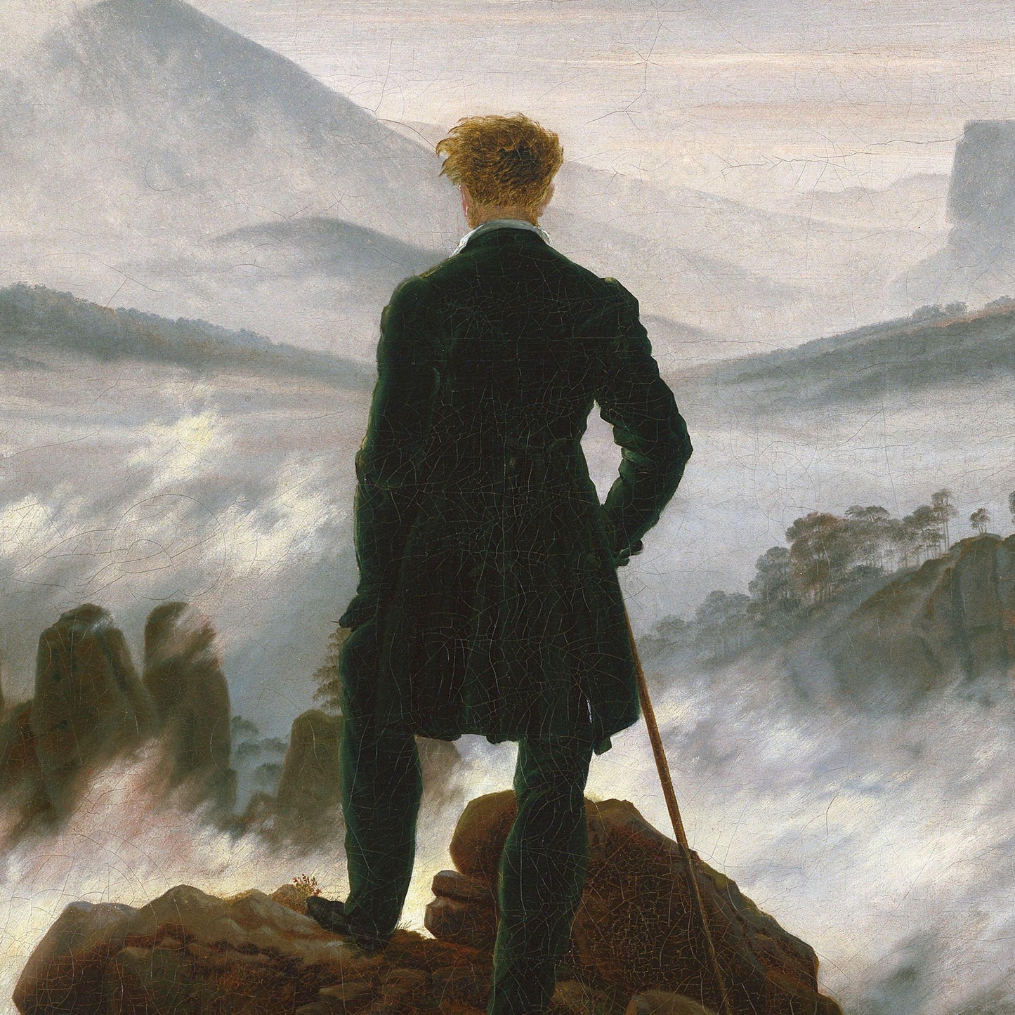 Man in a dark coat standing on a rocky outcrop with a landscape in the background