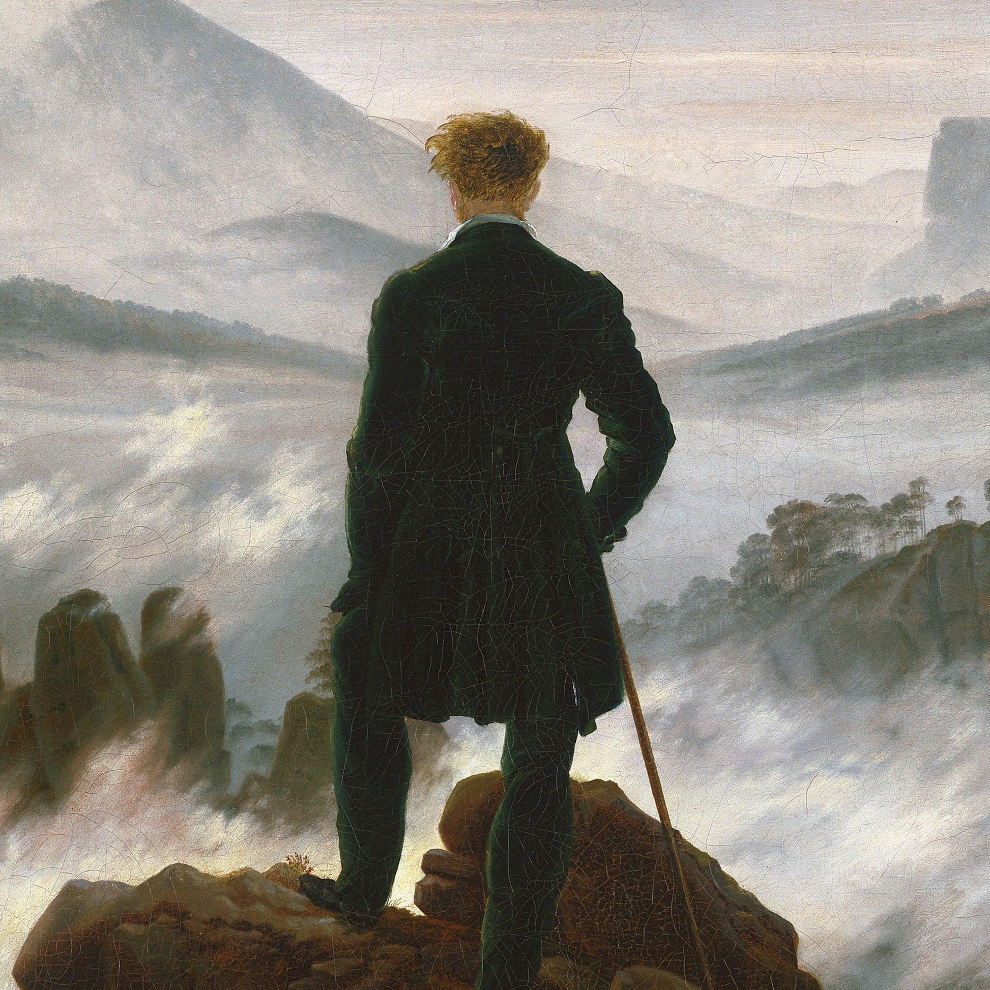 Man in a dark coat standing on a rocky outcrop with a landscape in the background