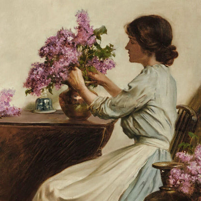 Woman arranging flowers in a vase with a still life of lilacs and vases on a table.